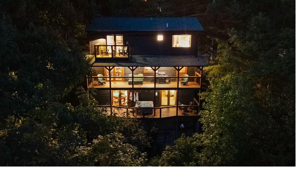 Aerial view of The Smoky Edit at night, its stacked decks lit warmly among dark trees